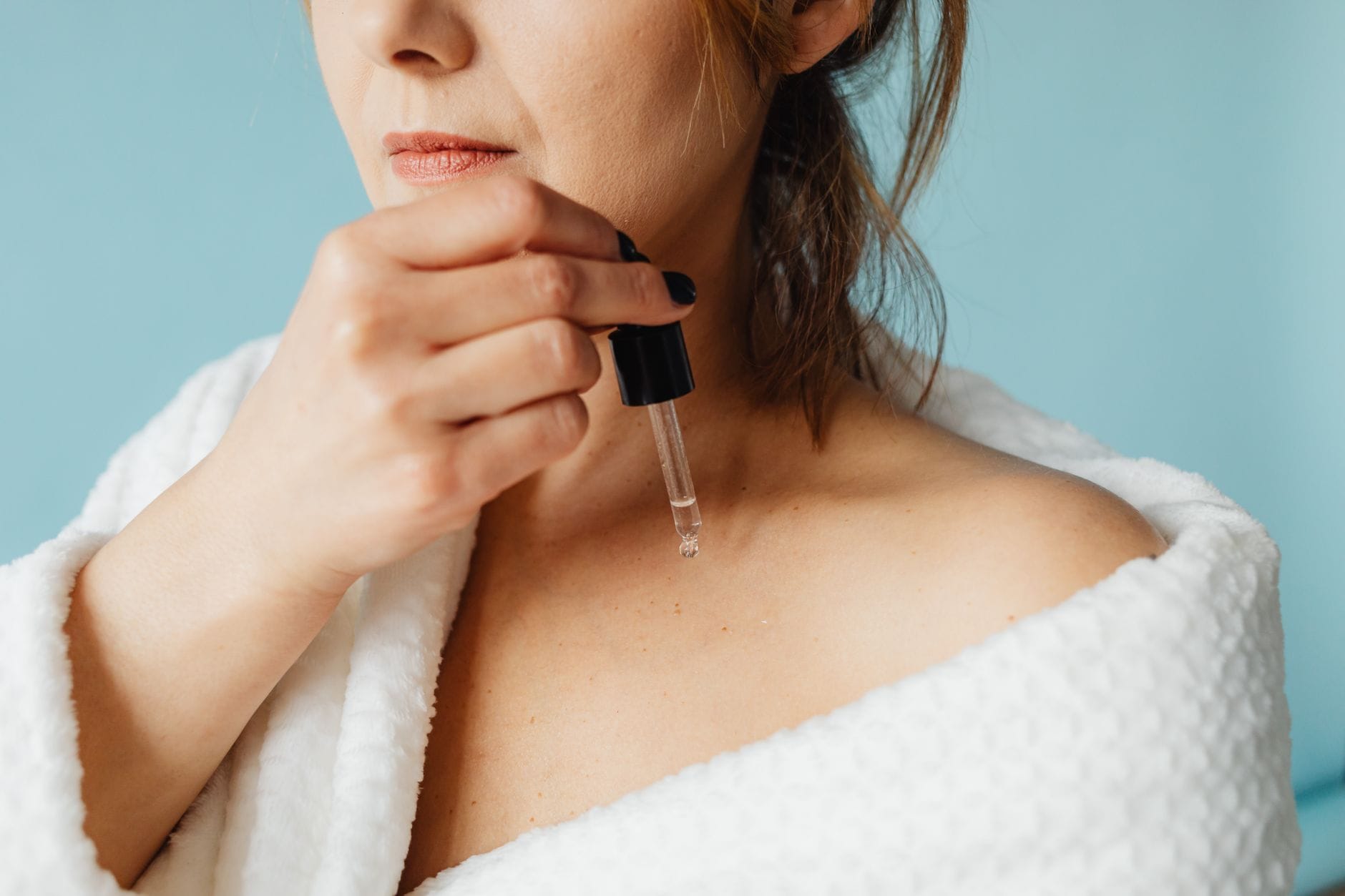 Kobieta w szlafroku nakłada serum na twarz w ramach pielęgnacji skóry