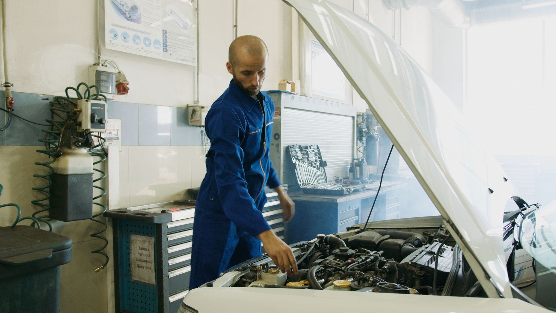 Mechanik w niebieskim kombinezonie sprawdza silnik auta w warsztacie
