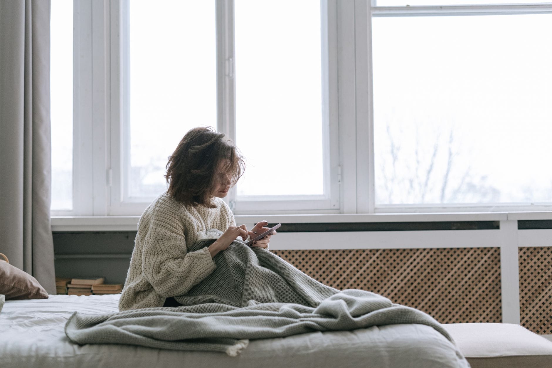 Kobieta w swetrze relaksuje się w łóżku, przeglądając telefon