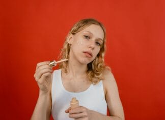7 błędów przy stosowaniu kwasu hialuronowego, przez które skóra staje się ściągnięta i sucha Kobieta nakłada serum z pipety na twarz na czerwonym tle