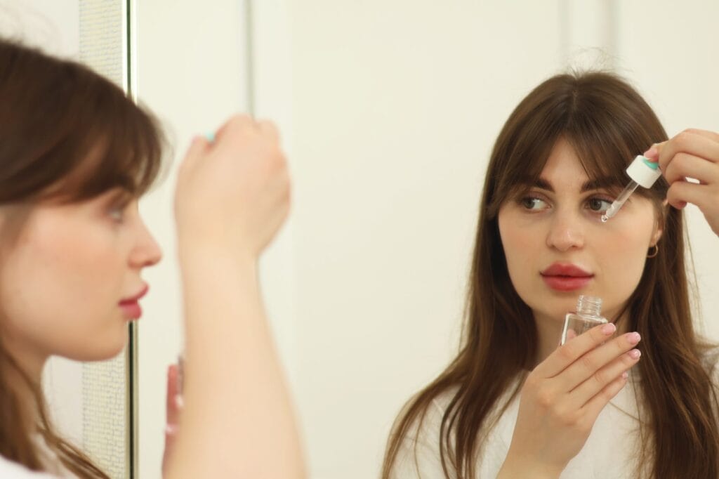 Młoda kobieta nakłada serum do twarzy przed lustrem